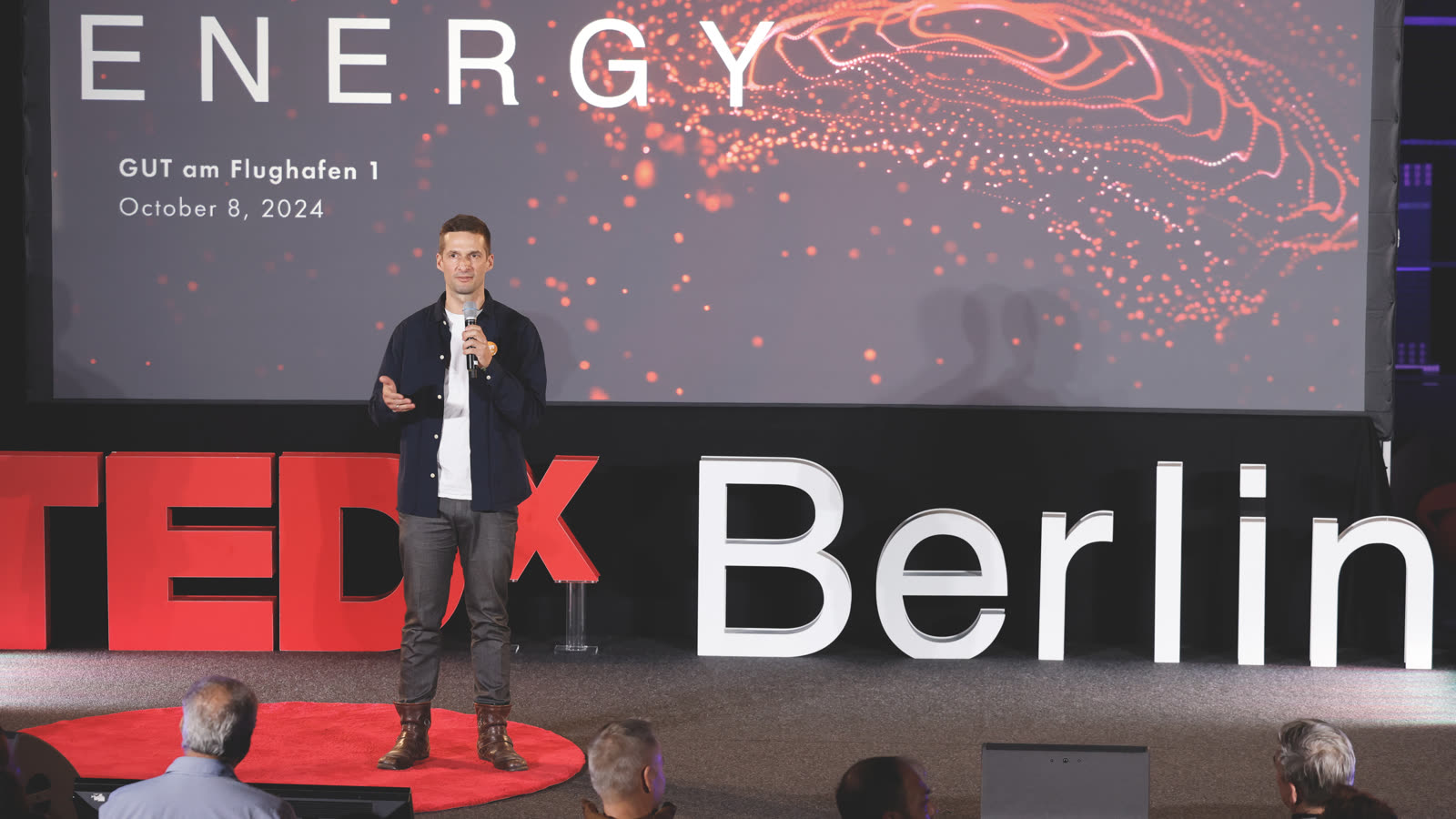 Marc Bernath mit Mikrofon auf der Bühne des TEDxBerlin Salon „The Future of Energy" vor dem Schriftzug TEDx Berlin